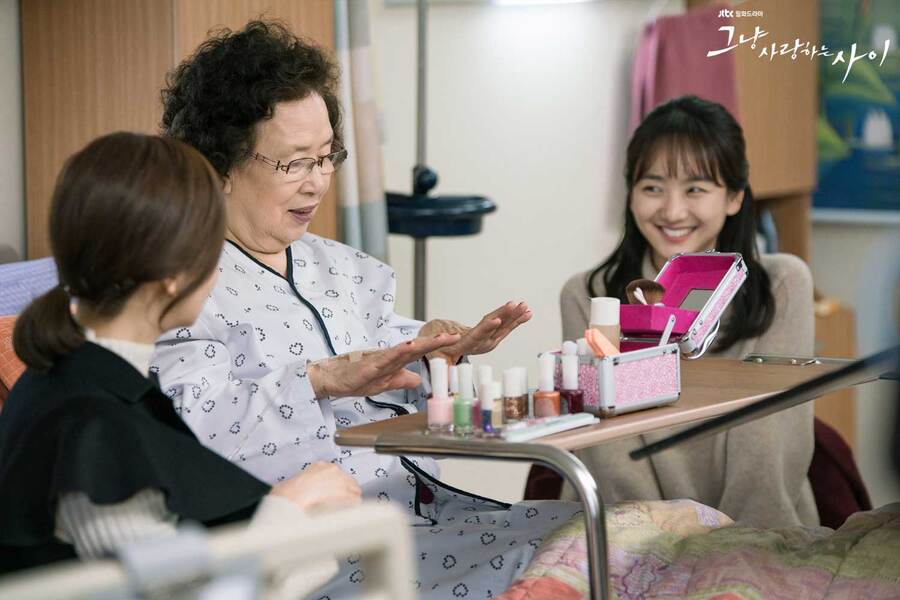 a scene from rain or shine kdrama where the grandma is sitting on her hospital bed, admiring her new nail polish while Moon-soo and Ma-ri look on and smile
